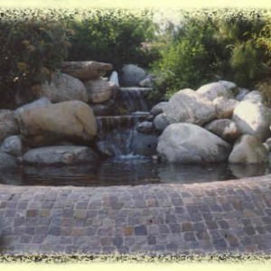 Brunnen mit Becken aus Natursteinpflaster, verziert durch kleine Quarzfindlinge
